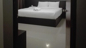 A hotel room with a large bed, a bedside table, a wall-mounted light, and a door with a number sign. - UD House (Udon Thani)