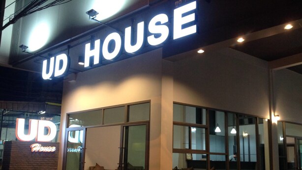 A UD House with a modern exterior, large glass windows, and a seating area visible inside. - UD House (Udon Thani)