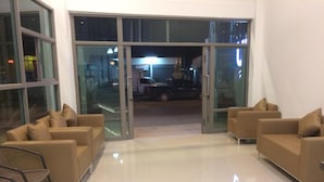 A lobby with two beige sofas, a glass door entrance, and a tiled floor. - UD House (Udon Thani)