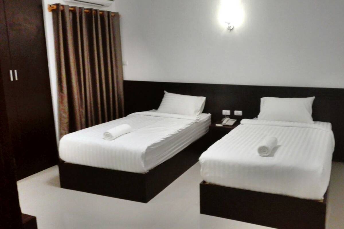 Habitación de hotel con dos camas individuales, cada una con edredón blanco y una toalla enrollada. Hay una mesita de noche con teléfono y lámpara entre las camas.