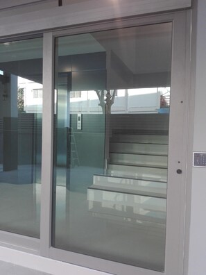 Entrada de un edificio moderno con puerta de cristal, escalera de metal y panel de alarma contra incendios visible.