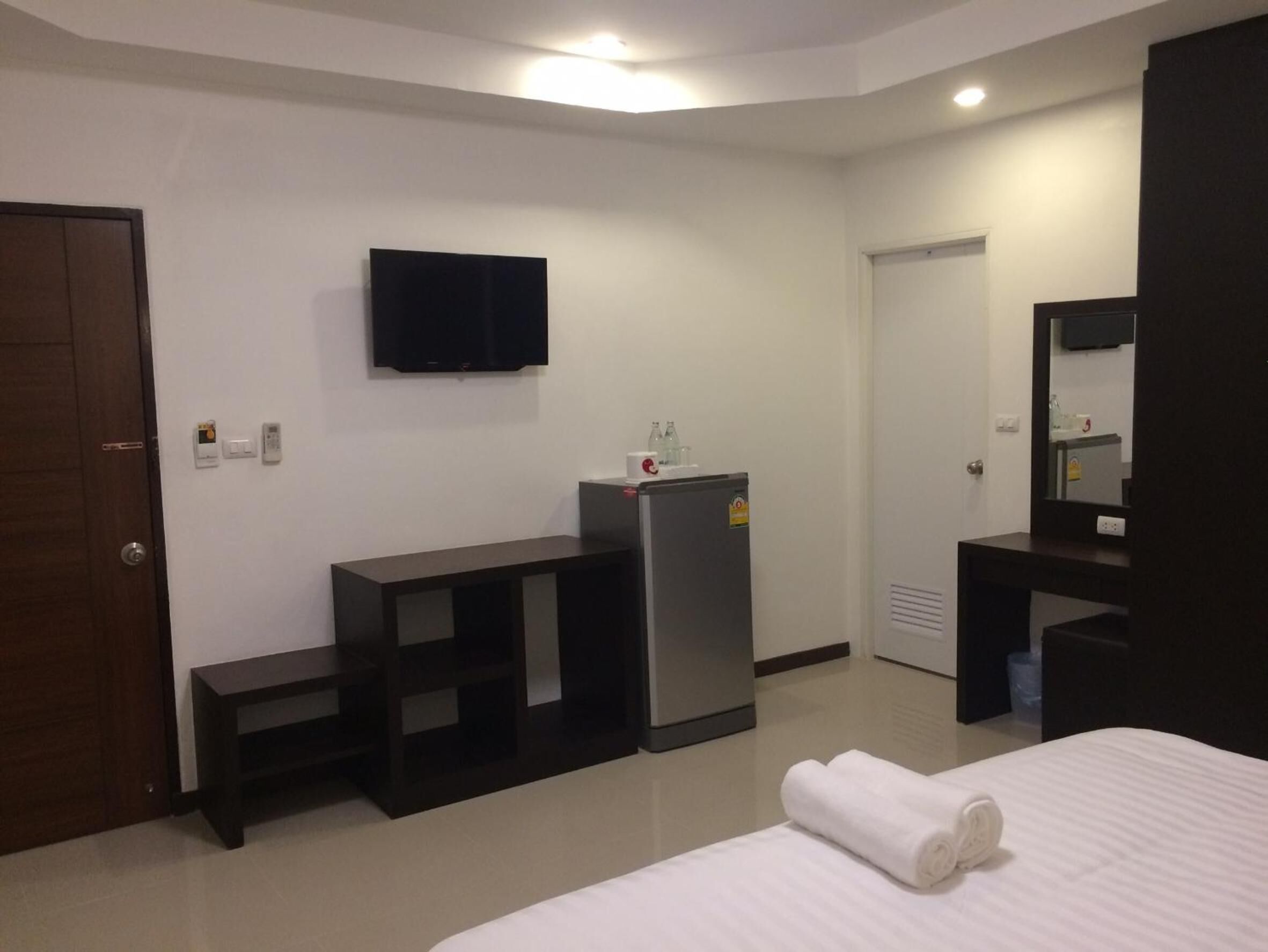 A hotel room with a bed, a TV mounted on the wall, a refrigerator, a desk, and a mirror.