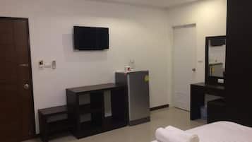 A hotel room with a bed, a TV mounted on the wall, a refrigerator, a desk, and a mirror.