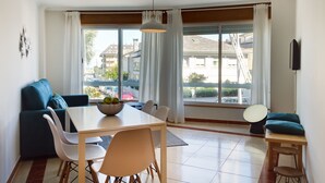 Una sala de estar moderna con una mesa de comedor, sillas, un sofá y vistas a la calle a través de amplias ventanas.