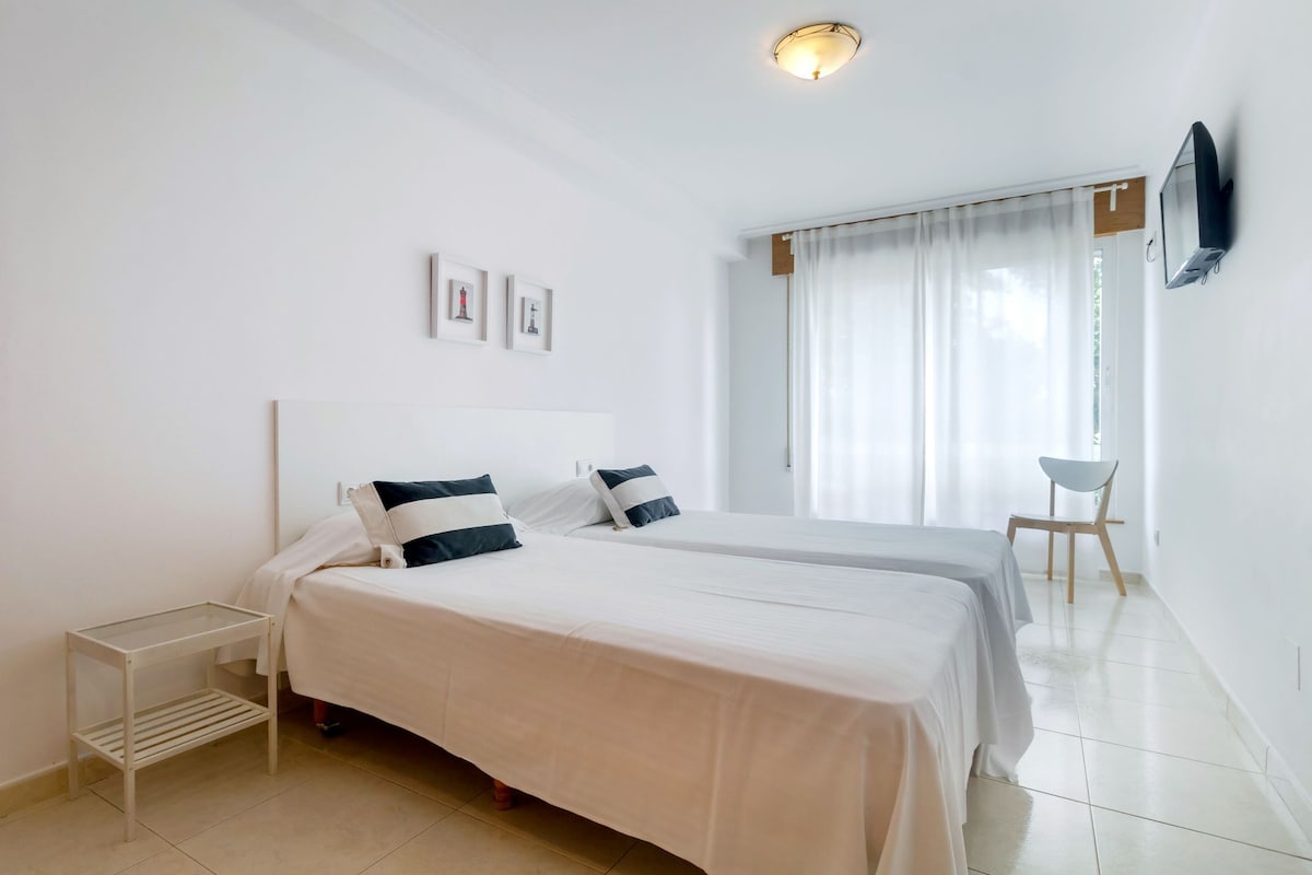 Habitación de hotel con cama, mesitas de noche, televisor en la pared y ventana con cortinas.