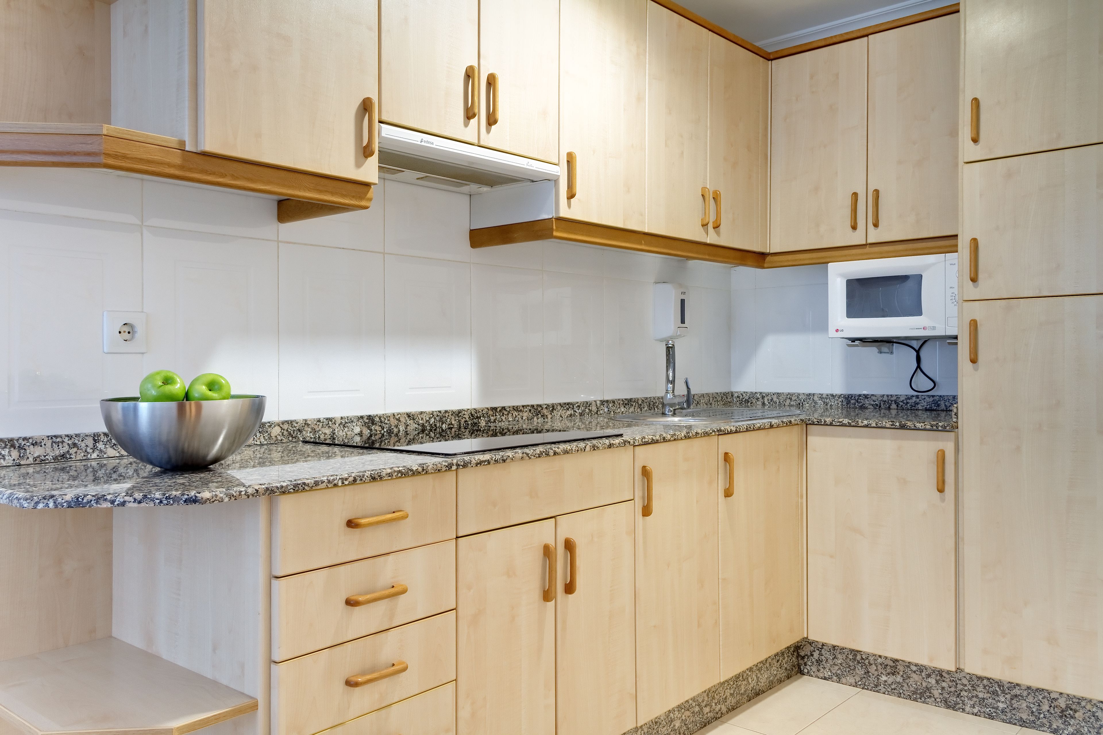 Cocina con armarios de madera, encimera de granito, pileta de acero inoxidable y un tazón de manzanas verdes.