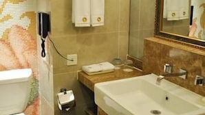 A bathroom with a toilet, sink, and mirror. There is a towel rack with towels, a trash can, and a small cabinet. - Junlin Dongfang Hotel (Zhenjiang)