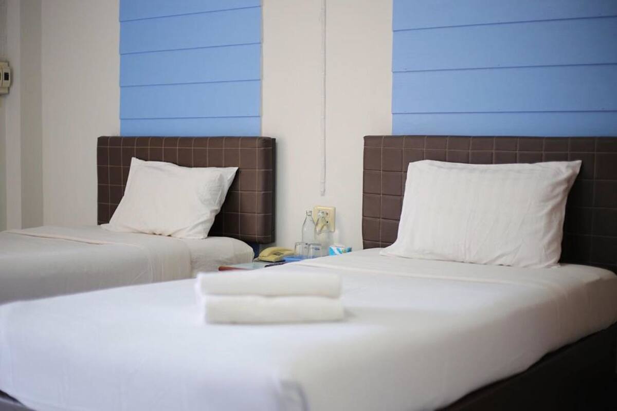 A hotel room with two beds, each with a brown headboard and white bedding. There is a telephone and a small table with a bottle and a glass on it.