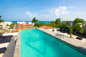 A swimming pool with a view of the ocean, surrounded by palm trees and lounge chairs.