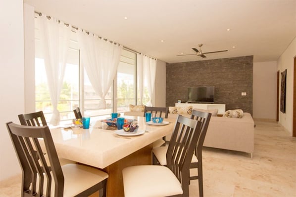 A modern dining area with a table set for four, a sofa, and a TV in the background.