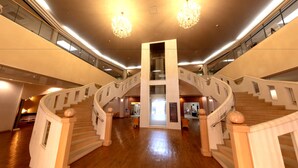A spacious interior with a central staircase flanked by glass railings, wooden flooring, and chandeliers.