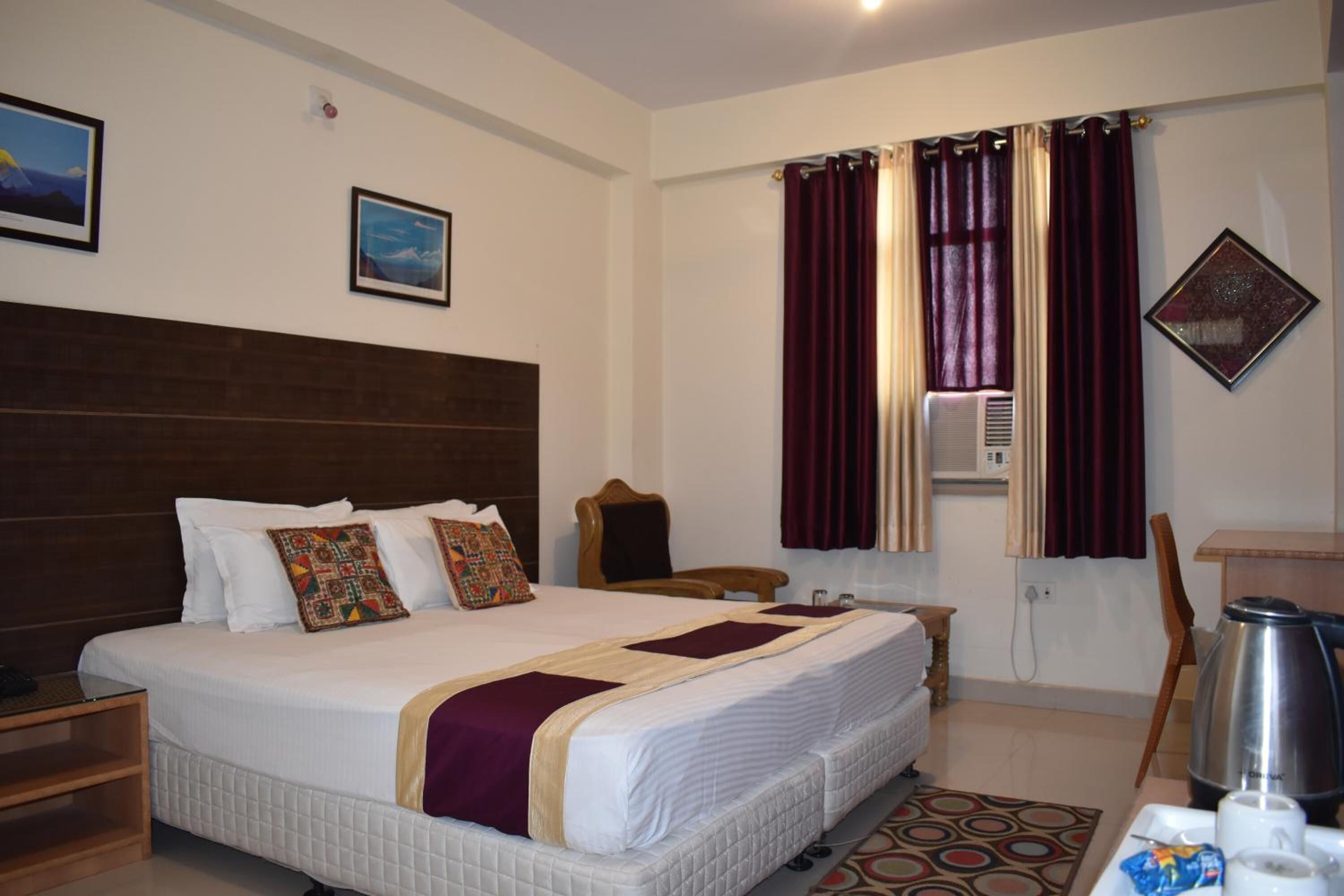 Habitación de hotel con una cama grande, cabecera de madera, escritorio con silla, cafetera y ventana con cortinas.