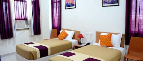 A hotel room with two beds, purple curtains, a wall-mounted air conditioner, and two framed pictures.