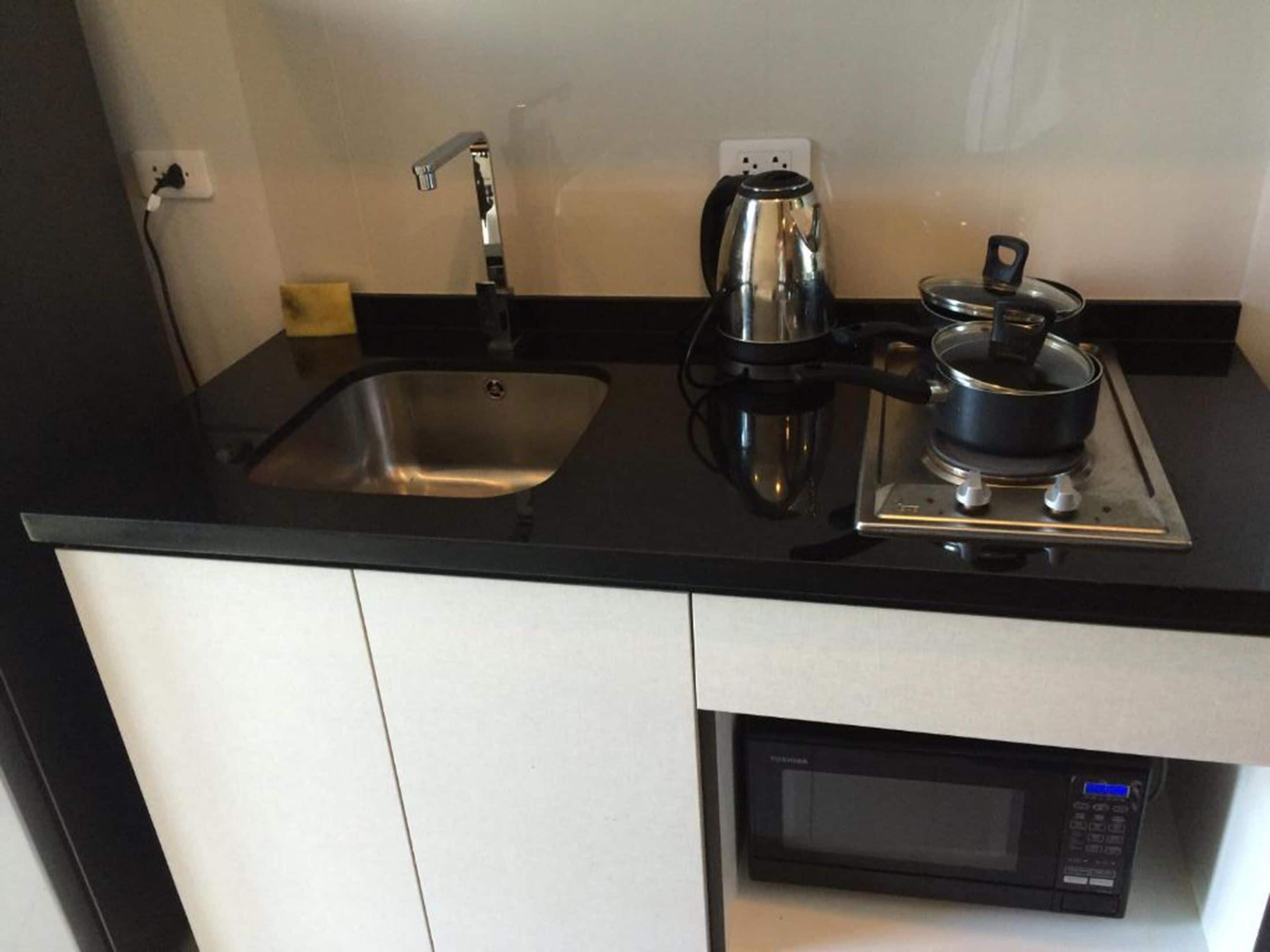 A kitchen with a sink, a kettle, a stove, and a microwave.