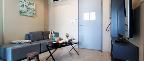 A living room with a grey sofa, a small wooden stool, a coffee table, and a flat-screen TV on a stand.