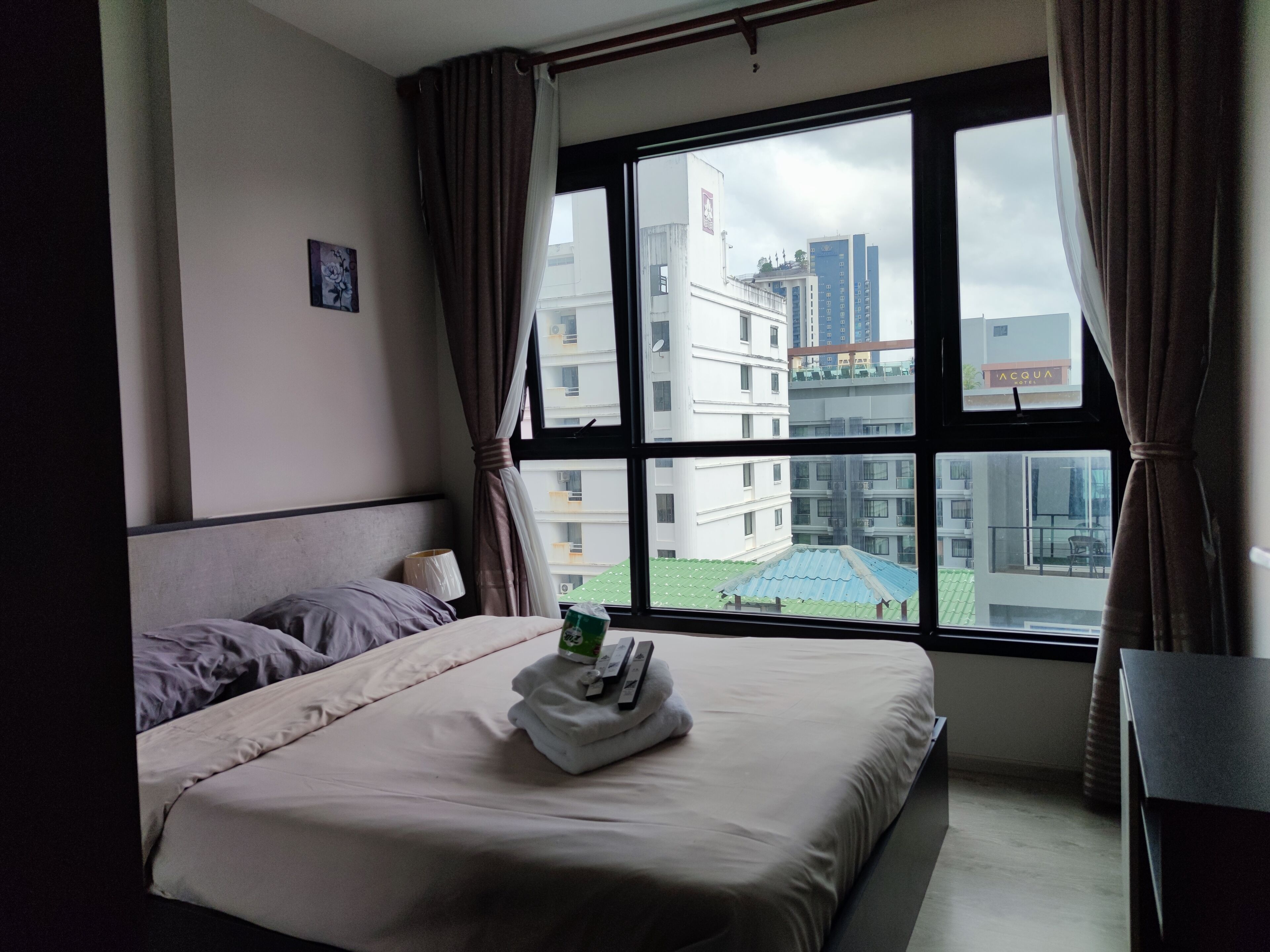 Habitación de hotel con una cama, ventana con cortinas y vistas a edificios, además de una pequeña mesa.