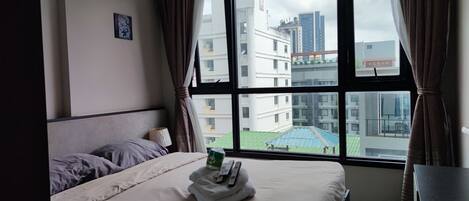 Habitación de hotel con una cama, ventana con cortinas y vistas a edificios, además de una pequeña mesa.