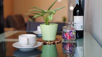 A table with a green plant in a pot, a bottle of wine, a glass jar with candy, and a white cup on a saucer.