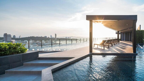 Ein Poolbereich auf dem Dach mit Blick auf die Skyline der Stadt, Treppen zum Pool und Liegestühle unter einer Pergola.