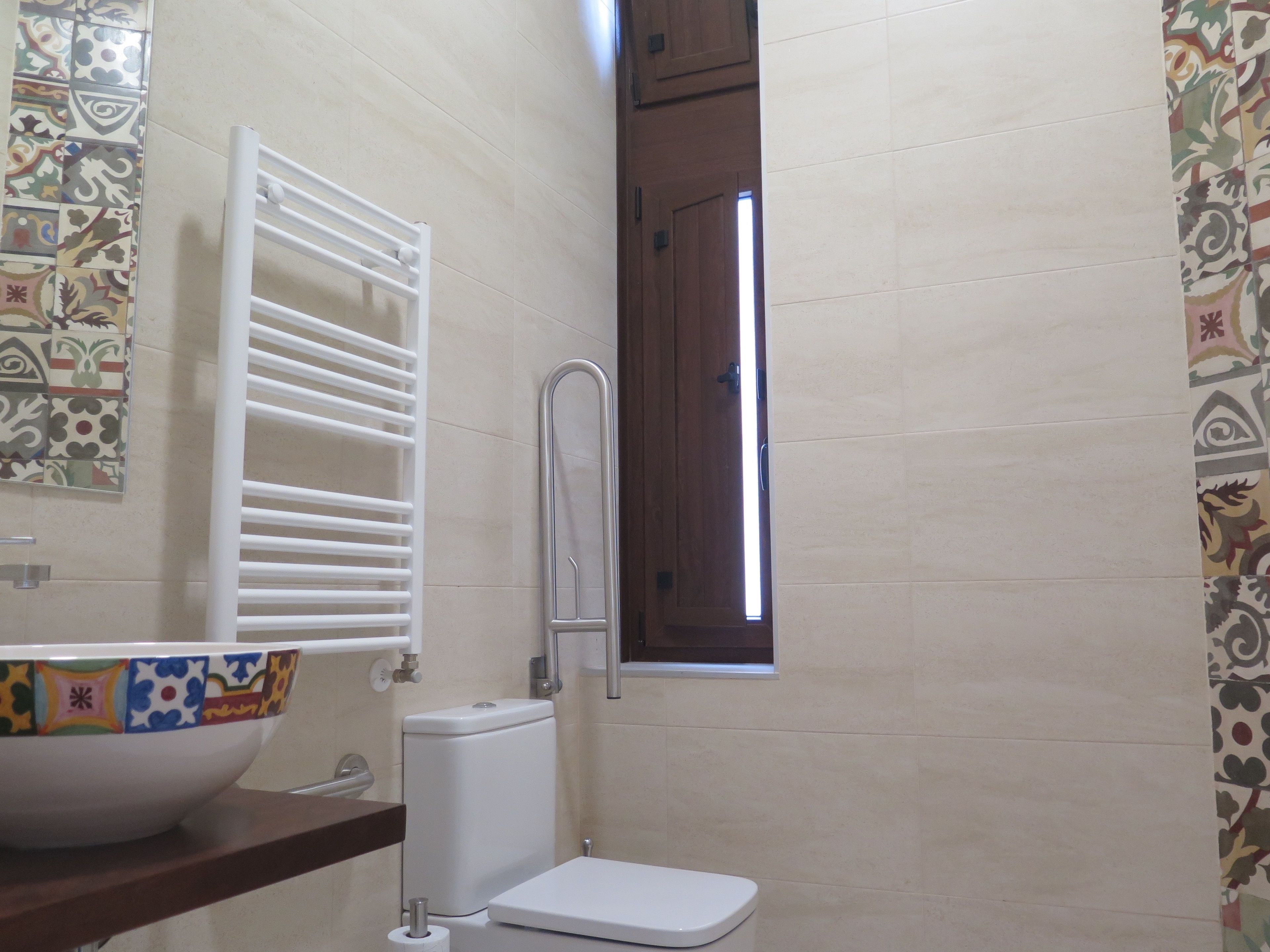Un baño con inodoro, lavamanos, toallero y ventana.