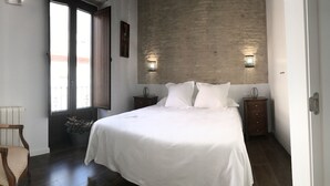 A bedroom with a large bed, a chair, a nightstand, and a wall-mounted light fixture. - Posada Pilatos (Seville)