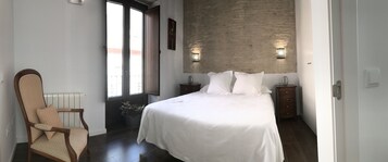 A bedroom with a large bed, a chair, a nightstand, and a wall-mounted light fixture.