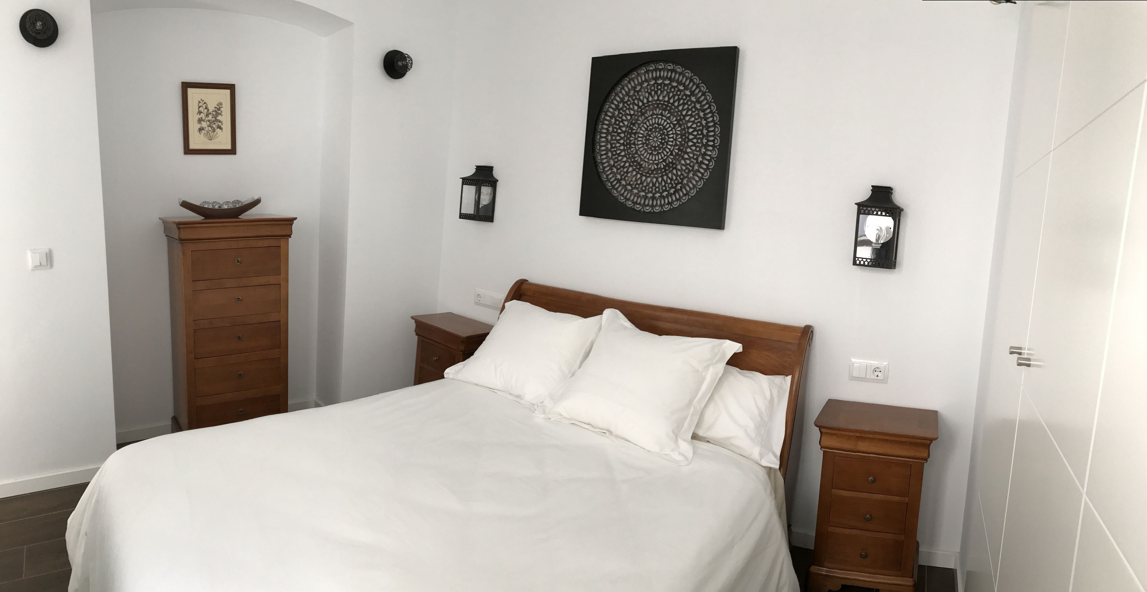 A neatly arranged bedroom with a bed, wooden nightstands, a dresser, and wall-mounted decor.