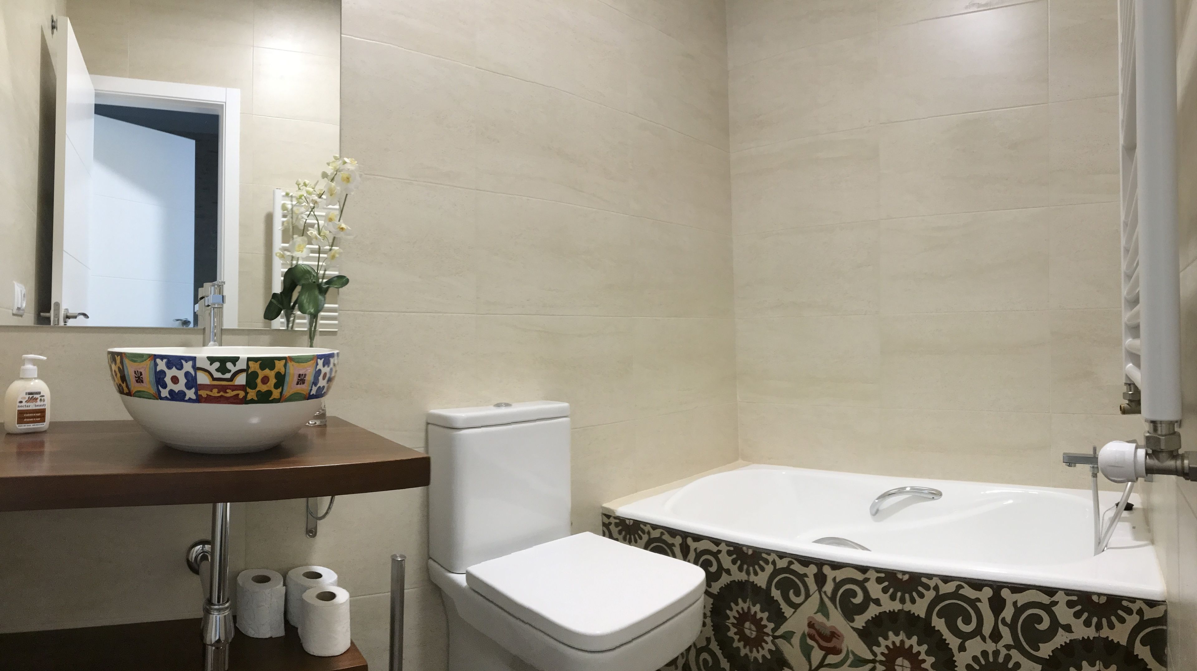 Une salle de bain avec des toilettes blanches, un lavabo blanc doté d’une cuvette colorée, une baignoire blanche et un miroir au-dessus du lavabo.