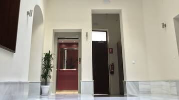 A hotel lobby with a marble floor, a potted plant, and a red door.