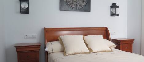 Un dormitorio con una cama de madera, dos mesitas de noche, un adorno en la pared y dos faroles de pared.