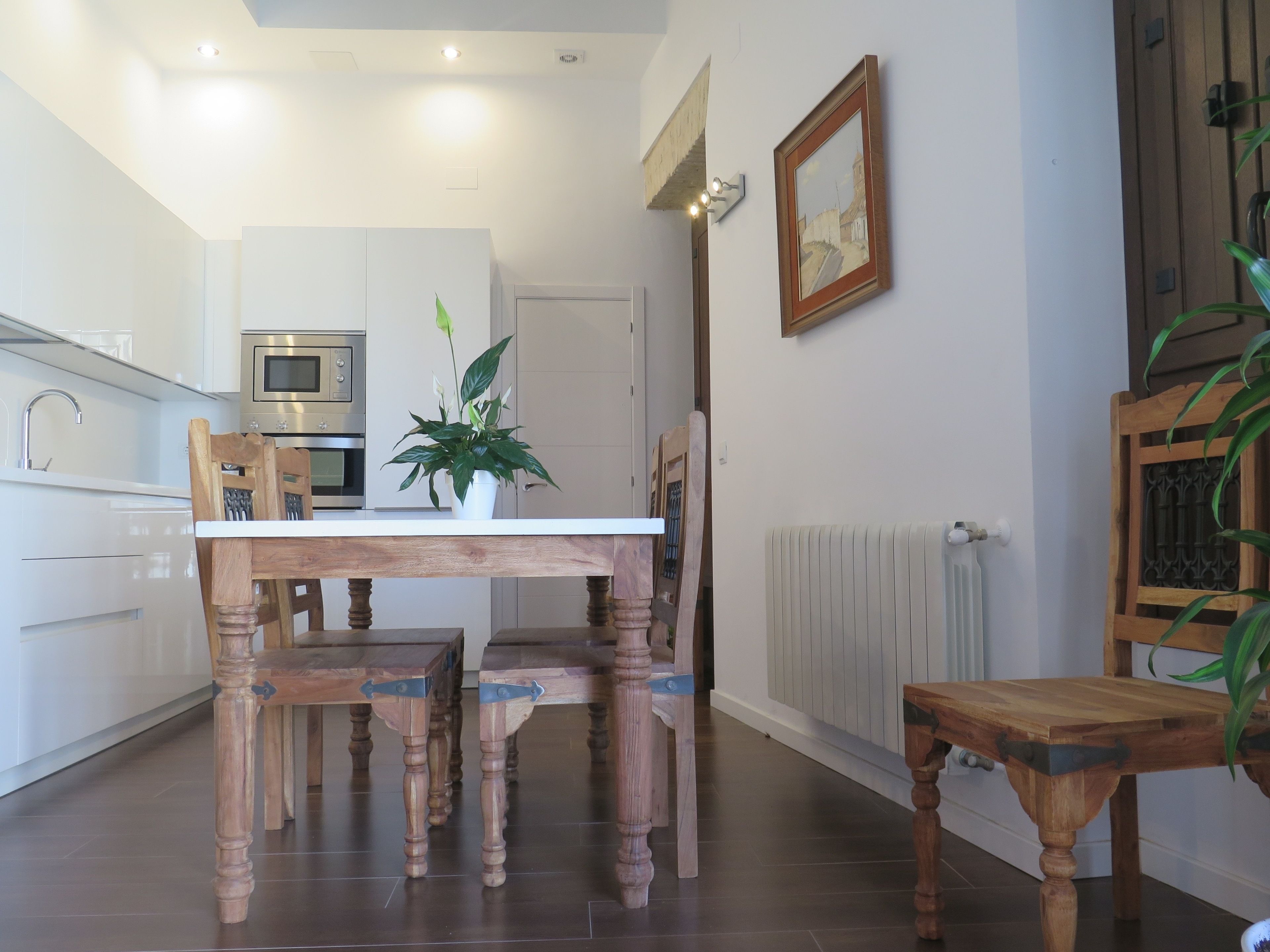 Una cocina moderna con armarios blancos, horno empotrado y una mesa de comedor con sillas de madera.