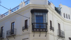 A white building with a large bay window and balconies with wrought iron railings. - Posada Pilatos (Seville)