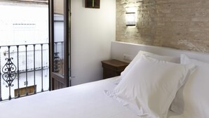 A hotel room with a bed, a nightstand, a wall-mounted light, and a balcony with a metal railing. - Posada Pilatos (Seville)