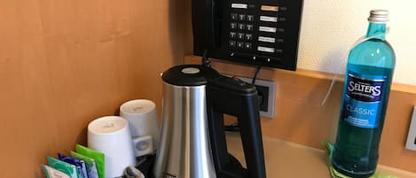 A coffee machine with a tray of condiments, a spoon, and a water bottle on a countertop.