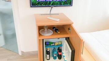 A room with a bed, a small wooden cabinet with a television mounted above it, and a mini-fridge with beverages.