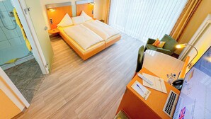 Hotelkamer met een tweepersoonsbed, een bureau met stoel, een douche en een groot raam met gordijnen.
