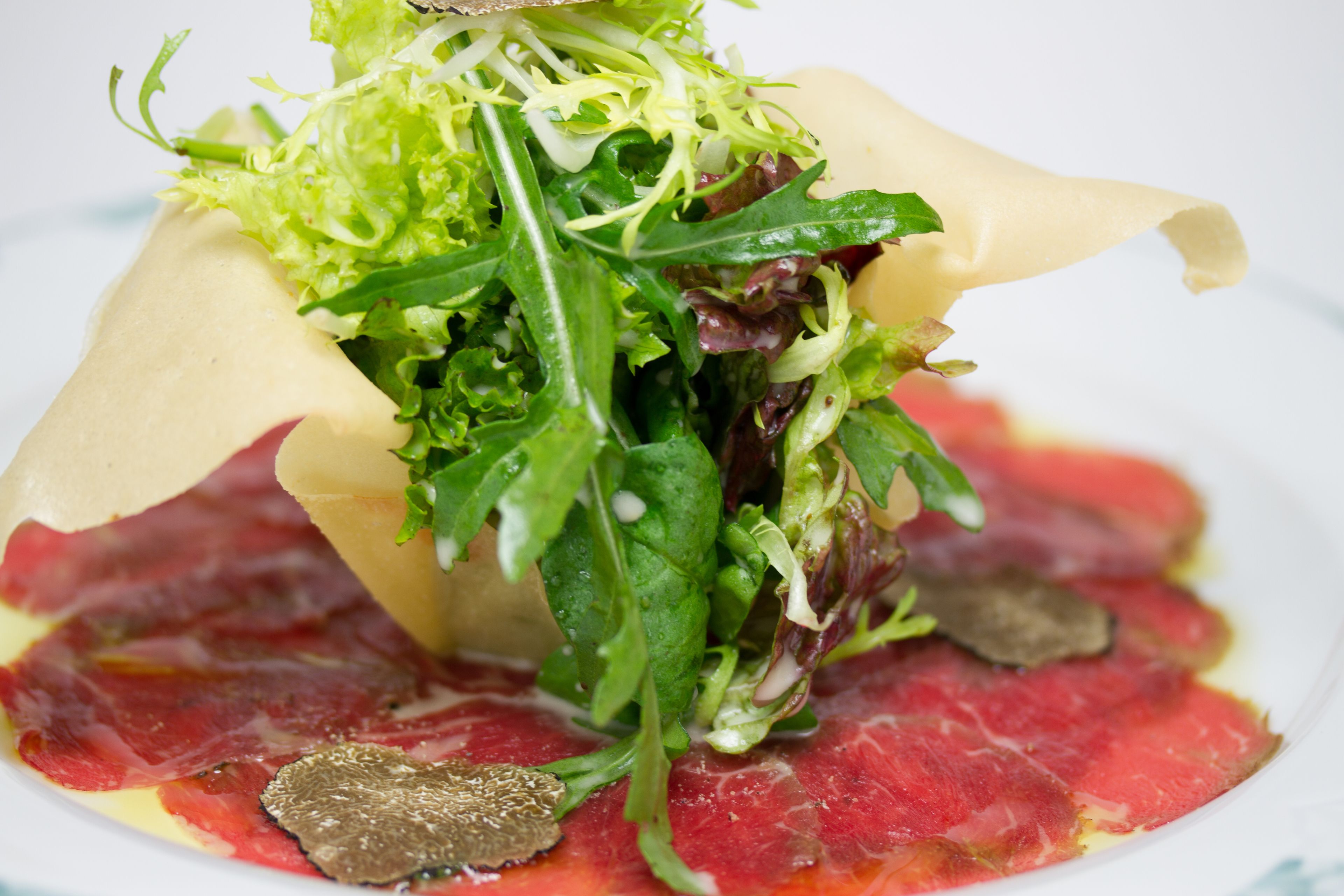 A dish with a variety of greens and a slice of red meat, possibly steak, on a white plate.