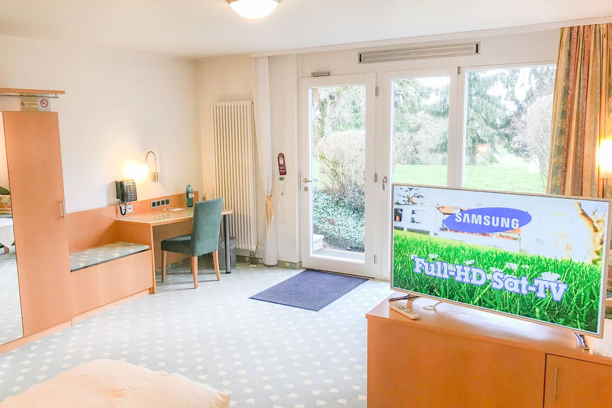 A hotel room with a bed, a desk, a chair, a television, and a view of the outdoors.