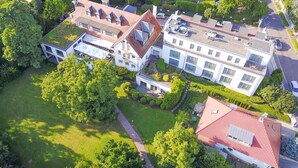 Luchtbeeld van een woongebied met meerdere huizen, waaronder een groot wit huis met een rood dak en een kleiner huis met een groen dak.