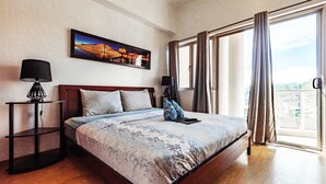 A hotel room with a large bed, two bedside tables, a nightstand, a window with curtains, and a cityscape view.