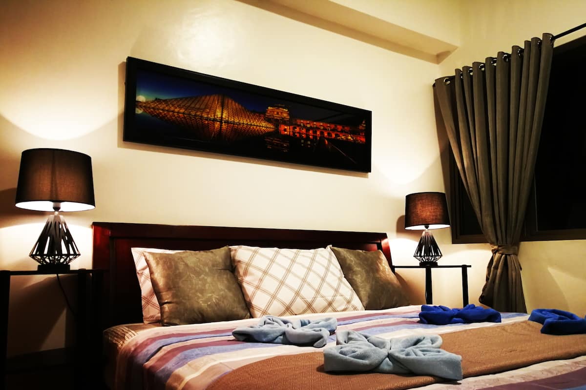 A hotel room with a bed, two bedside lamps, a framed picture on the wall, and a window with curtains.
