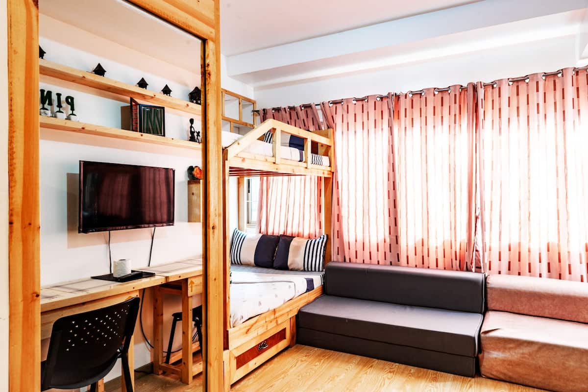 A room with a bunk bed, a desk with a computer, a chair, and a sofa.