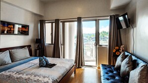 A bedroom with a bed, a sofa, a TV, and a balcony with a view.