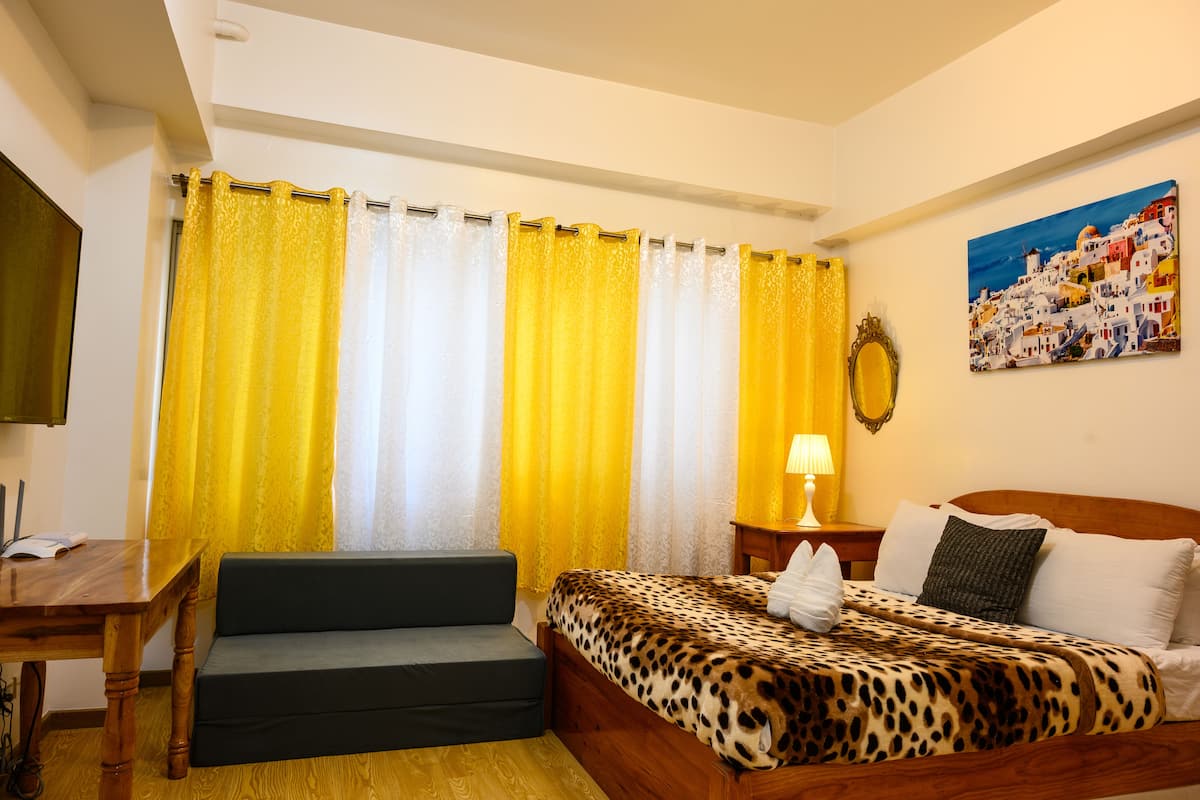 A bedroom with a bed, a sofa, a table, and a painting on the wall.