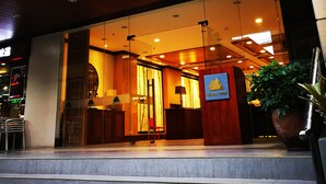 A hotel entrance with a modern design, featuring a glass facade, a wooden reception desk, and a sign indicating a nearby attraction.