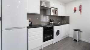 Una cocina moderna con armarios blancos, horno empotrado, microondas y lavadora.