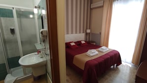 A hotel room with a bed, a bedside table, a mirror, a sink, and a shower. - Abacus (Reggio Calabria)