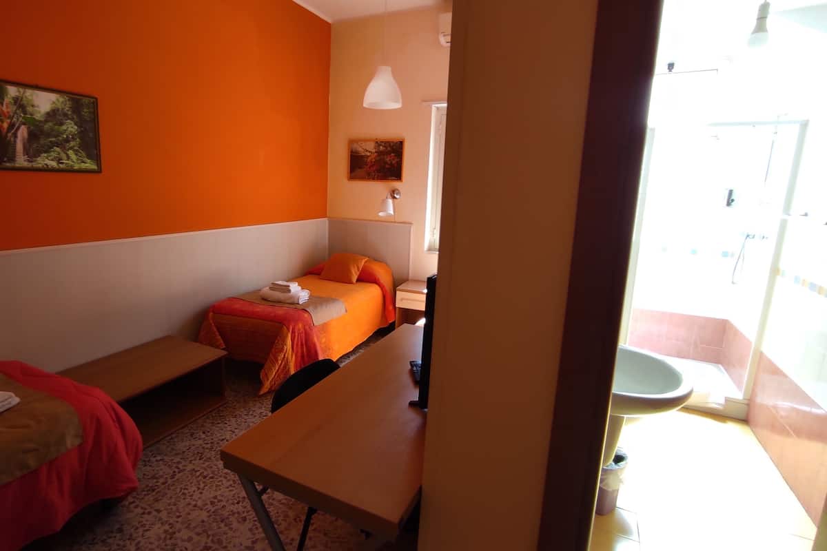 Hotellihuone, jossa on kaksi erillistä sänkyä, pieni pöytä, penkki, työpöytä ja kylpyhuone, joka näkyy avoimesta ovesta.