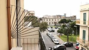 A balcony with a metal railing overlooking a street with parked cars and buildings in the background. - Abacus (Reggio Calabria)