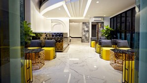 Um lobby moderno com piso de mármore, áreas de estar em amarelo e preto, e um balcão de recepção central.